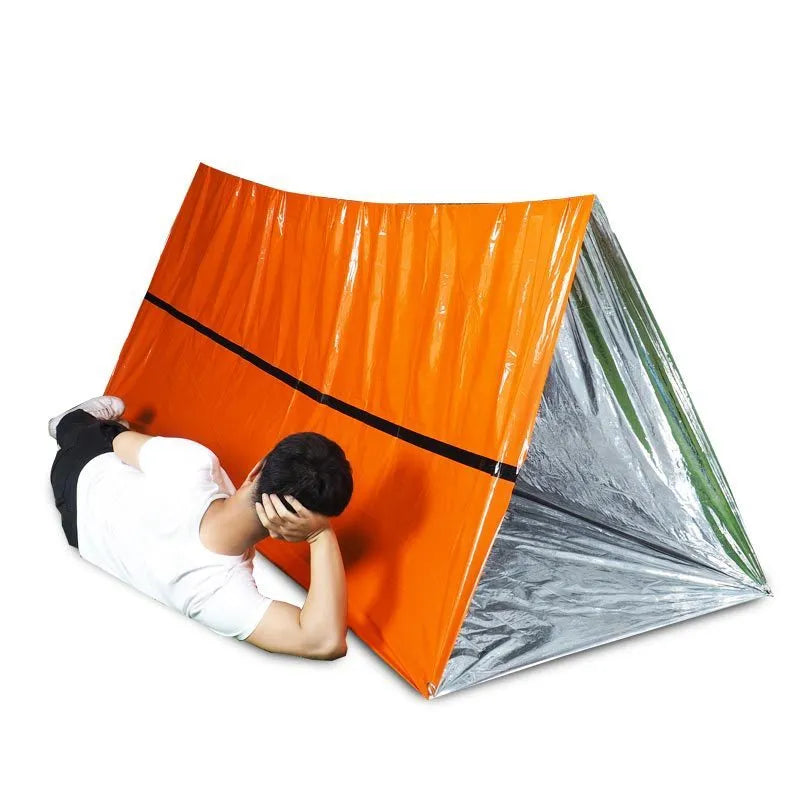 Orange emergency survival blanket unfolded showing reflective inner surface, with folded sleeping bag and tent beside it in nylon bag