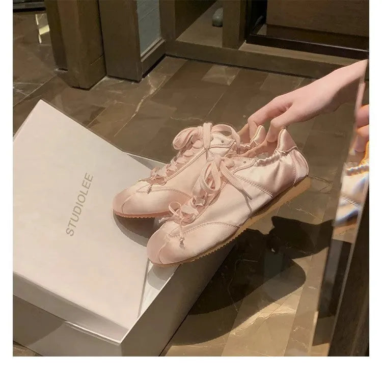 Women's silver grey satin ballet flats with round toe and white lace-up front on a plain background.