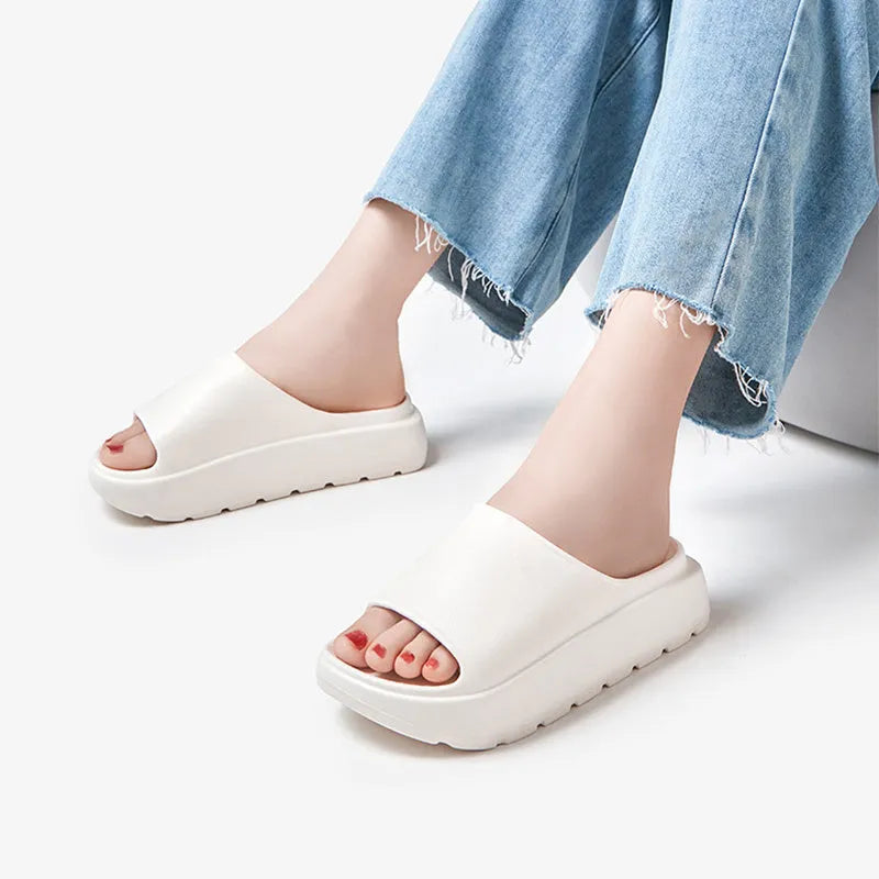 Women's beige thick-soled beach slippers with a fish mouth design on a wooden floor.