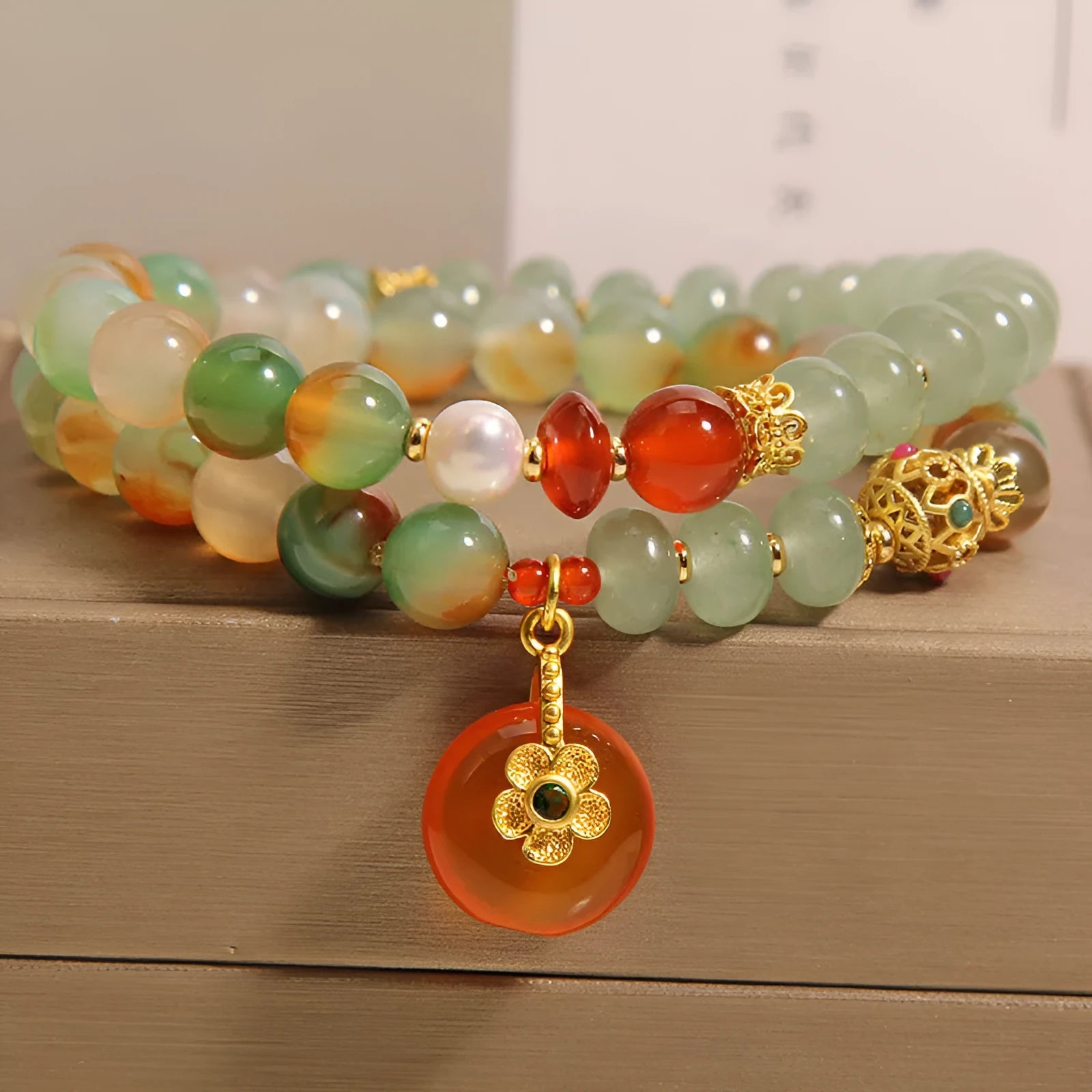 Gold-toned double ring chain bracelet with a peacock green agate safety buckle pendant and rhinestone details.