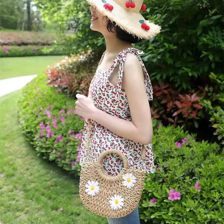 Light brown woven straw crossbody bag with daisy decoration showing shoulder strap