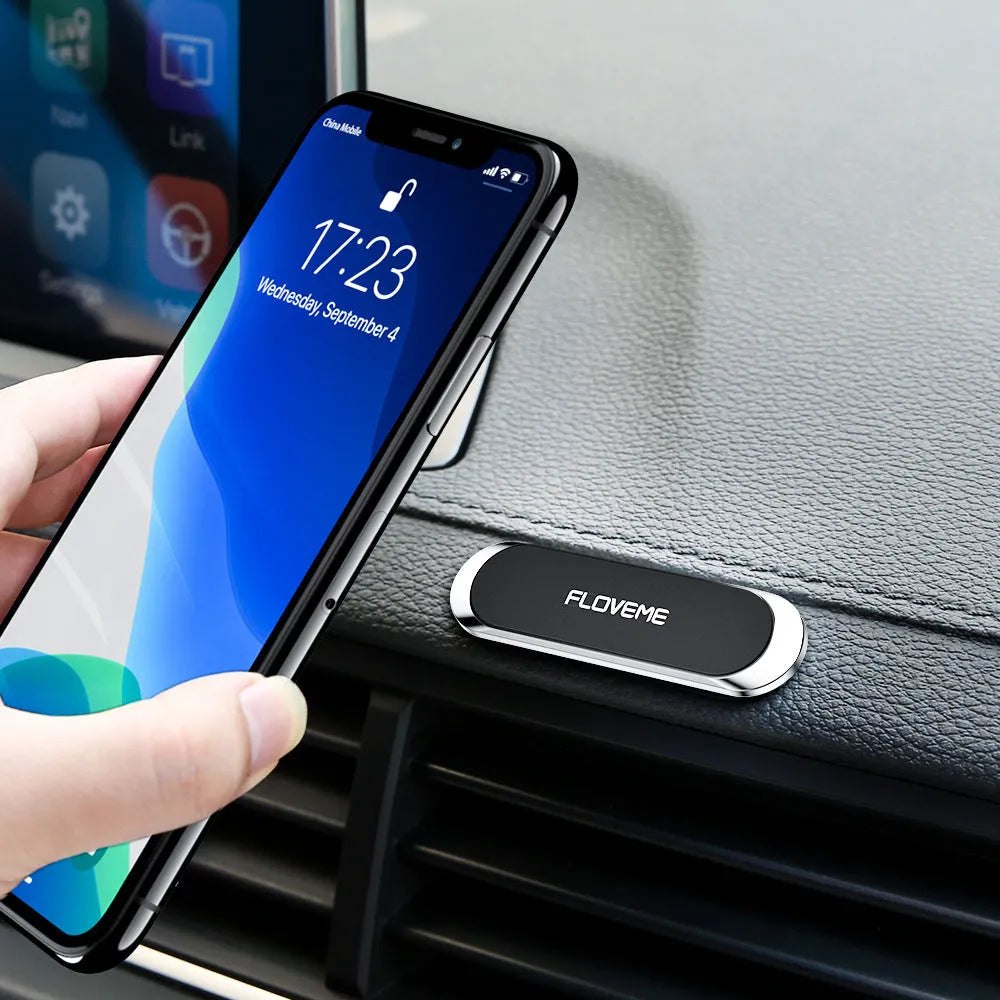 Black magnetic car phone holder with silver iron plate and white adhesive, shown next to a mobile phone.