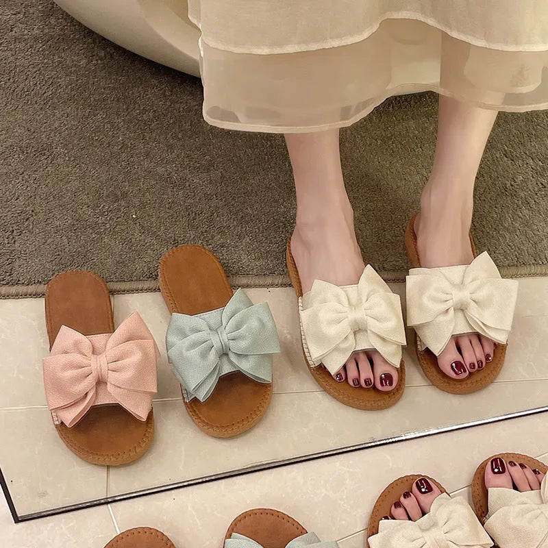 Women's beige suede slip-on sandals with a bow detail and a flat rubber sole.