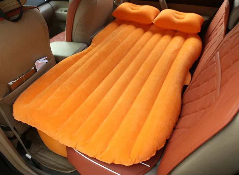 Black inflatable car bed with flocked material set up in the back of a five-seater vehicle, showing two pillows.