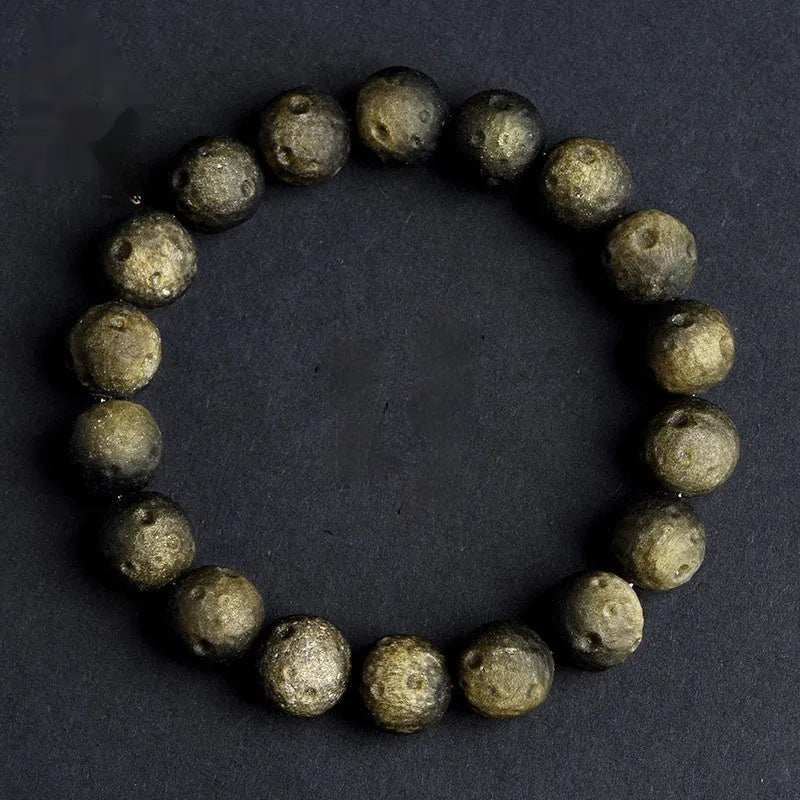 Natural obsidian crater ball bracelet with a ground texture in silver stone or gold colours on a wrist.