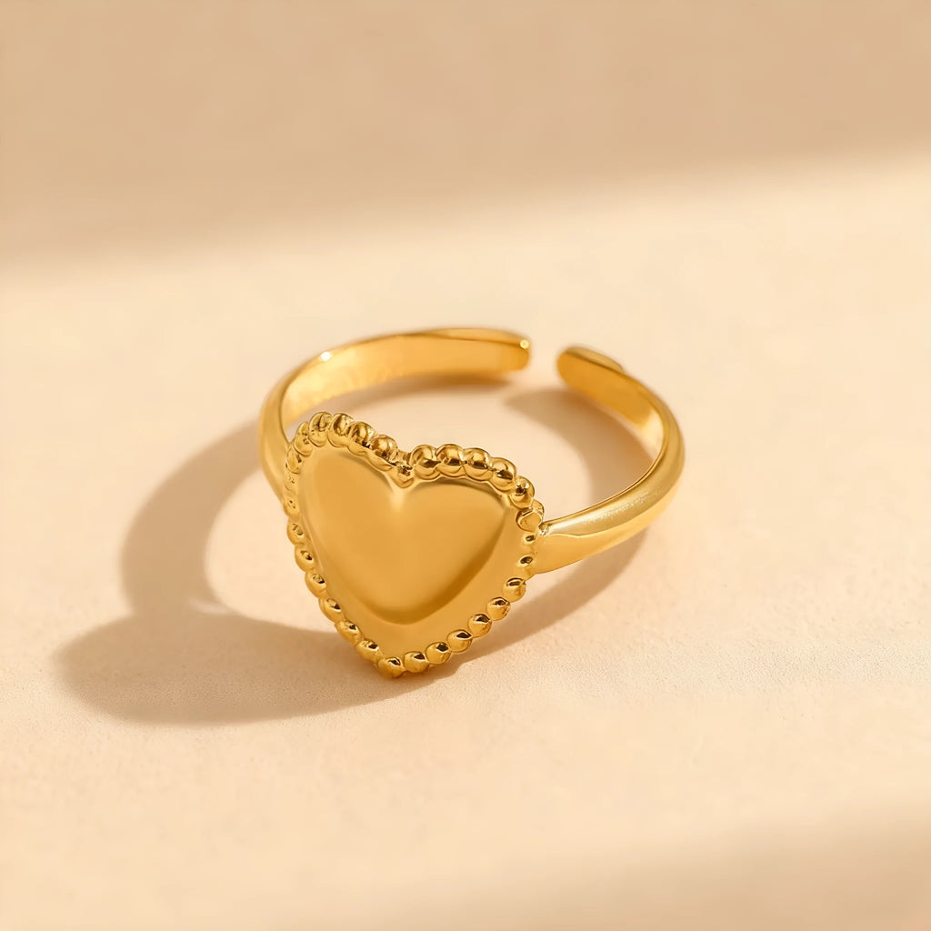 Adjustable stainless steel heart ring with electroplated gold finish on plain background