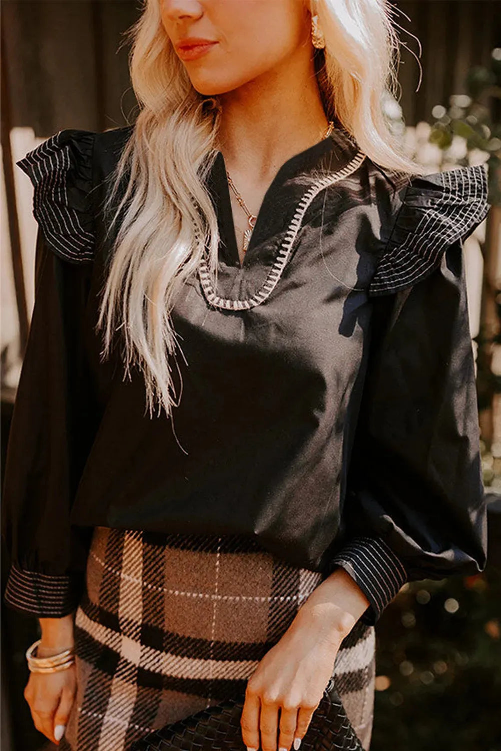 Black women's V-neck blouse with ruffled long sleeves and contrast stitching.