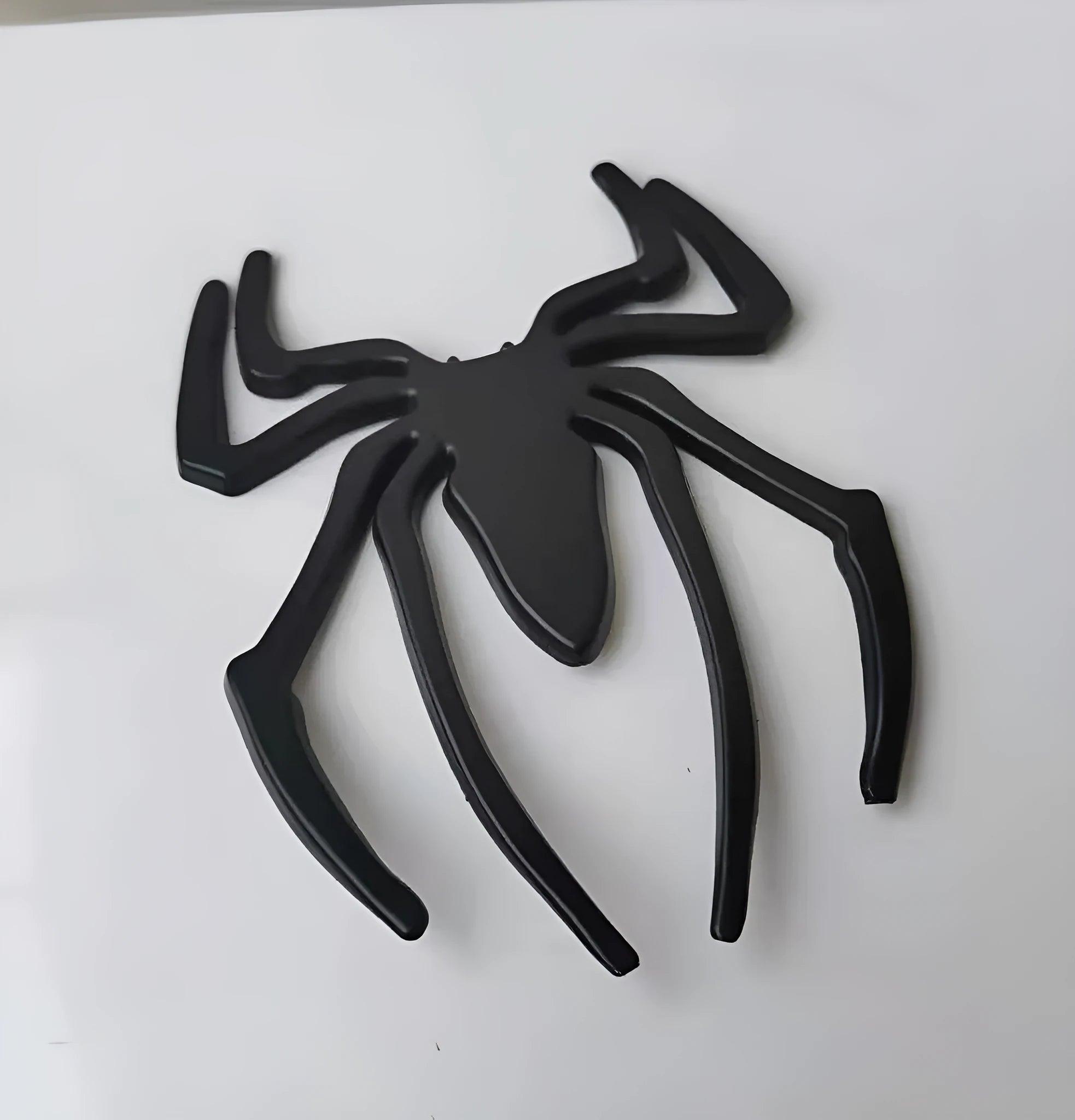 Three-dimensional metal spider bumper sticker in metallic finish.