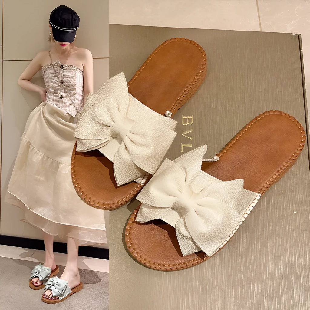 Women's beige suede slip-on sandals with a bow detail and a flat rubber sole.