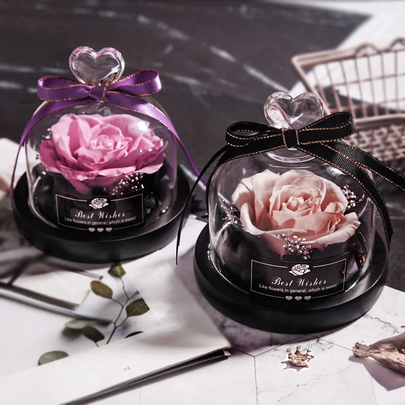 Eternal preserved red rose illuminated by LED light inside a clear glass dome on a wooden table.