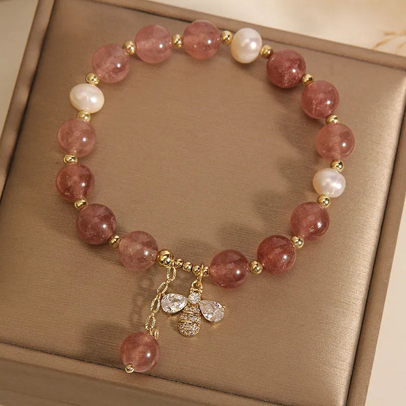 Close-up of a women's bracelet with pink strawberry quartz beads, white freshwater pearls, and sparkling zircon charms on an alloy chain.