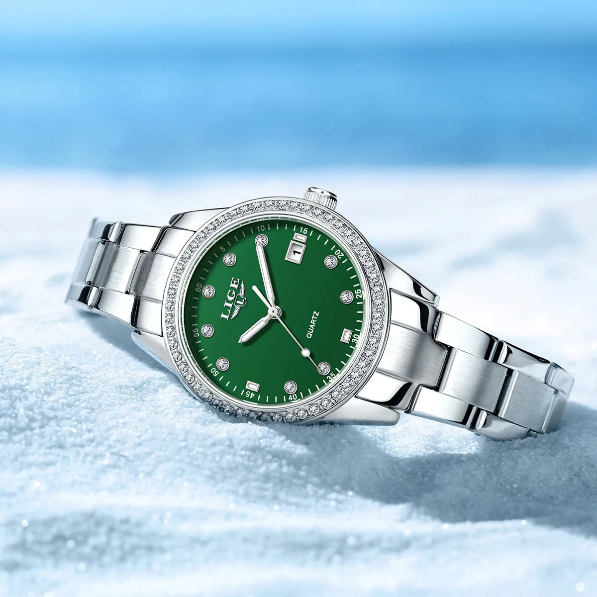 Women's silver and green quartz watch with diamond bezel, luminous hands, on a wrist.