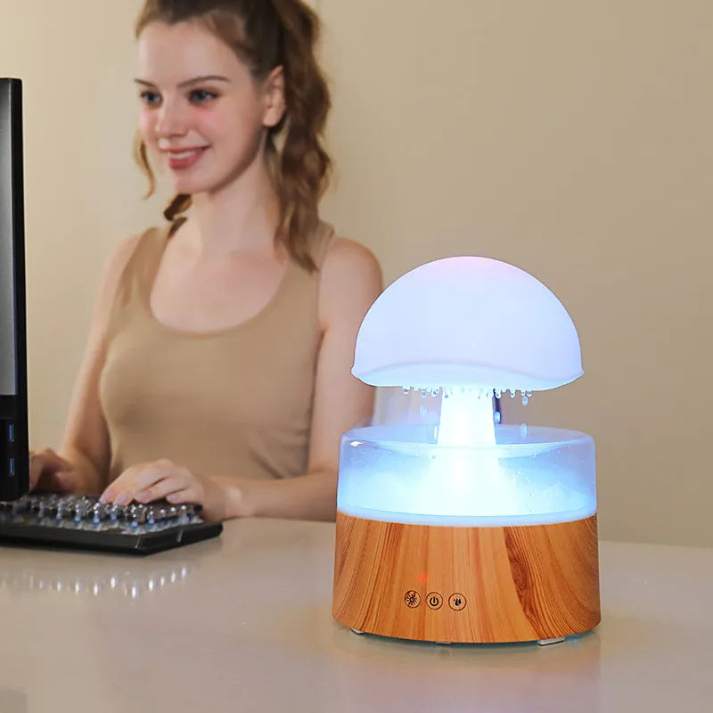 White rain cloud shaped ultrasonic humidifier and aromatherapy diffuser with coloured lights on a wooden table.