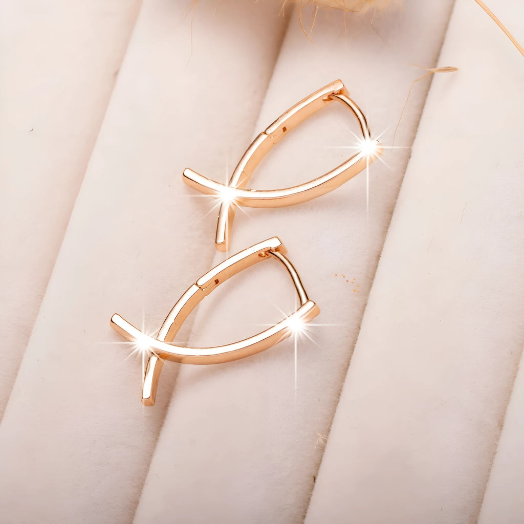 A pair of rose gold cross shaped drop earrings on a plain background.