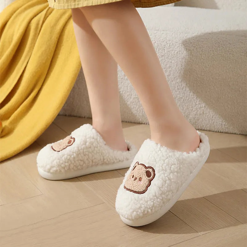 Pair of cute cartoon bear winter slippers with plush upper and non-slip TPR sole on a bedroom floor