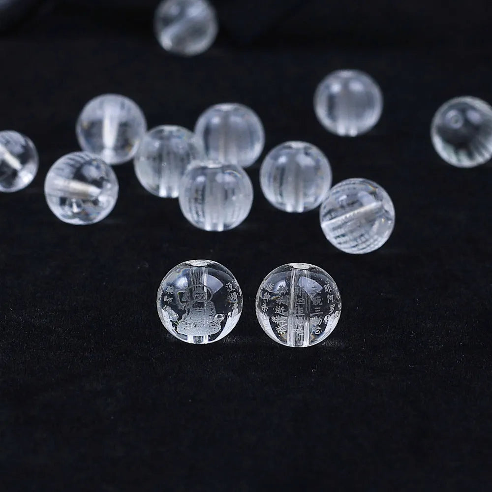 Ten 10mm round crystal prayer beads with Heart Sutra design, polished glass finish, scattered on a surface.