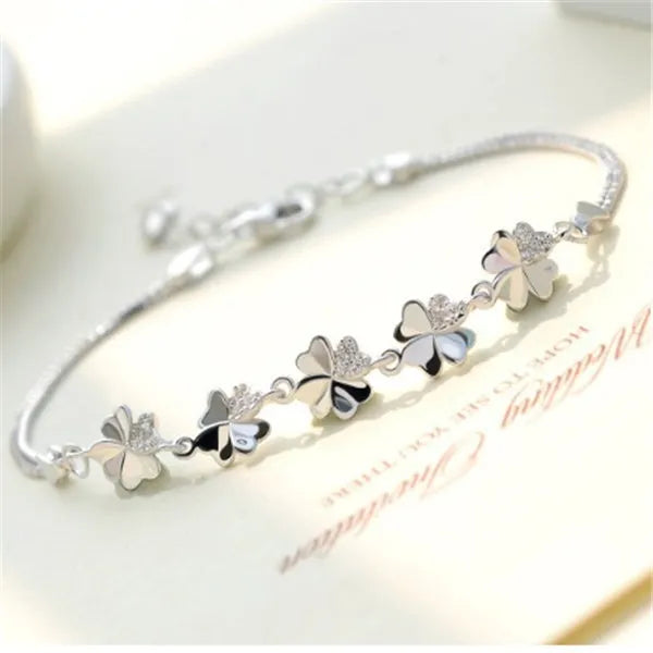 Silver four-leaf clover bracelet with leaf pendant on a plain background