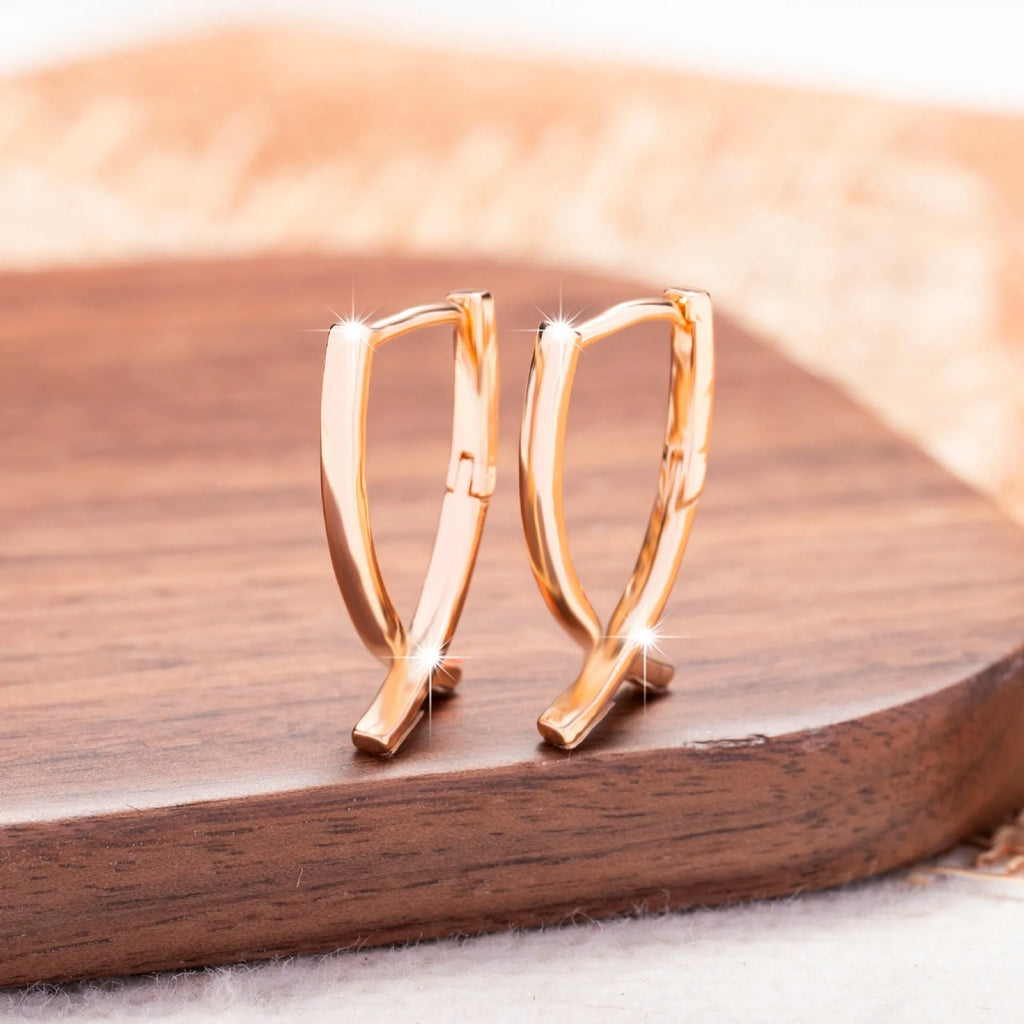 A pair of rose gold cross shaped drop earrings on a plain background.