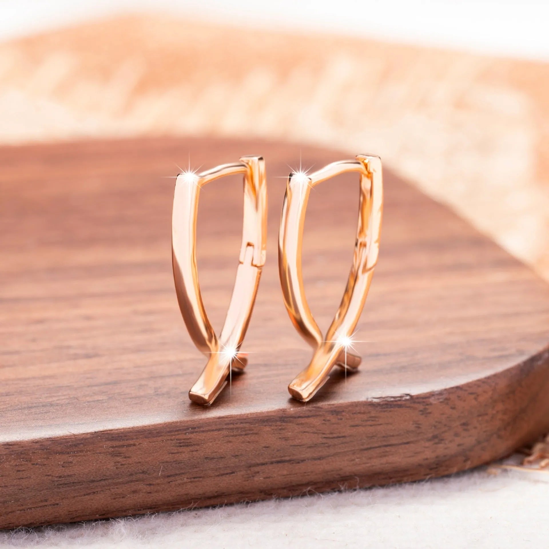 A pair of rose gold cross shaped drop earrings on a plain background.