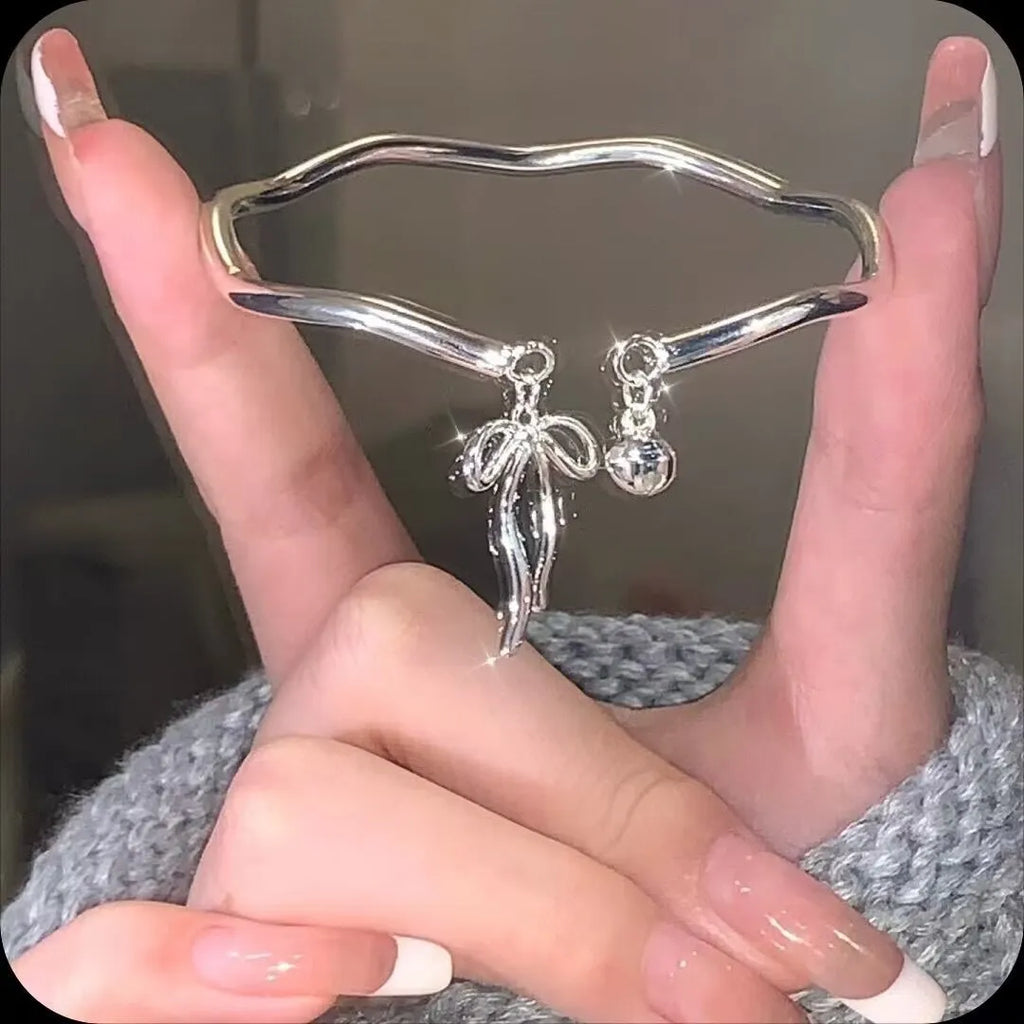 Silver adjustable bow bracelet with a bell opening clasp on a wrist.