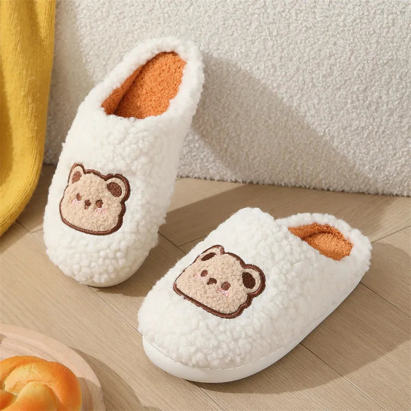 Pair of cute cartoon bear winter slippers with plush upper and non-slip TPR sole on a bedroom floor