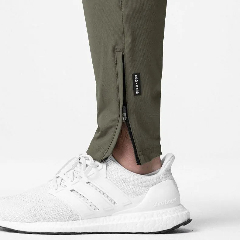 Men's loose grey fitness trousers with elasticated ankle ties on a gym floor.
