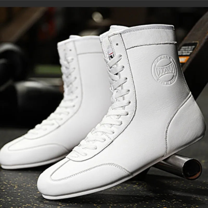 Pair of black and gold professional boxing shoes with mesh panels on a gym floor.