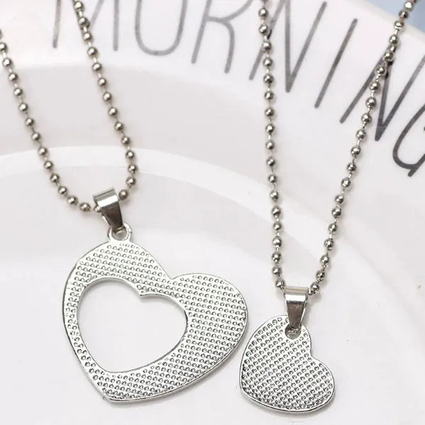 Two matching silver heart-shaped cross chain necklaces on a surface, alloy construction