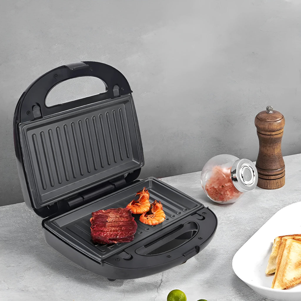 Black electric sandwich pan with double-sided heating and stainless steel lid on a kitchen counter.
