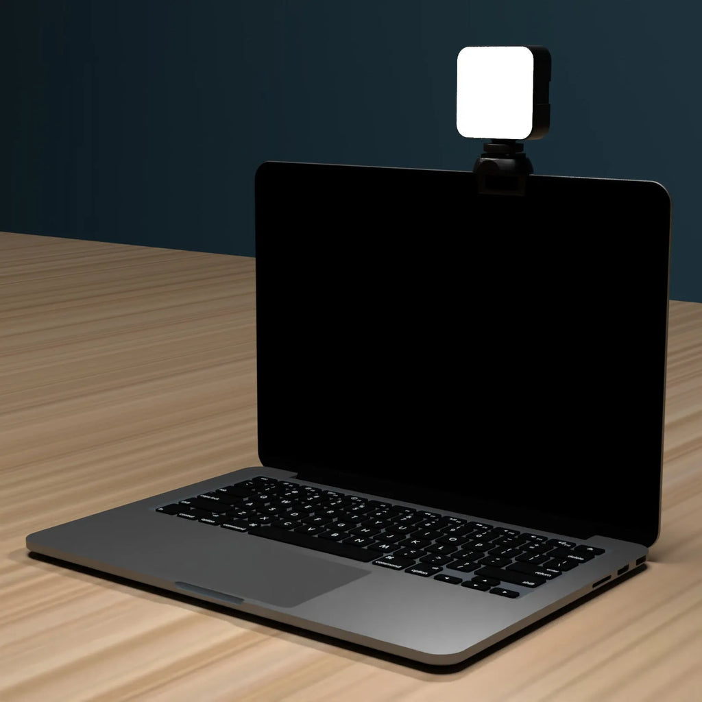 Silver 5600K LED video light cube clipped onto a laptop, with shelf and wire included