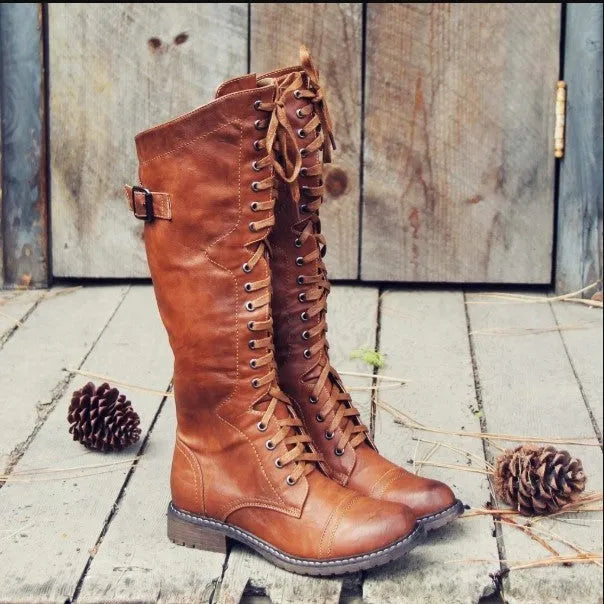 Women's black knee-high knight boots with a cross strap detail across the ankle.