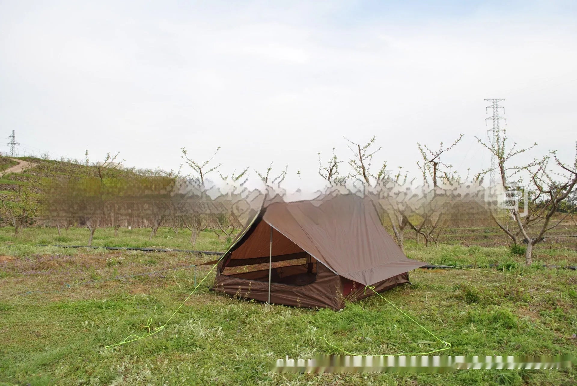 Lightweight brown A-line hiking tent set up with hiking cane supports in outdoor setting