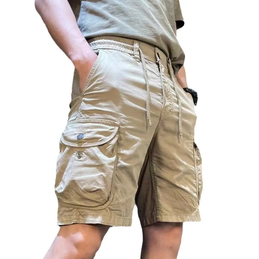 A pair of loose-fitting, straight-leg multi-pocket overalls trousers in a khaki colour on a model.