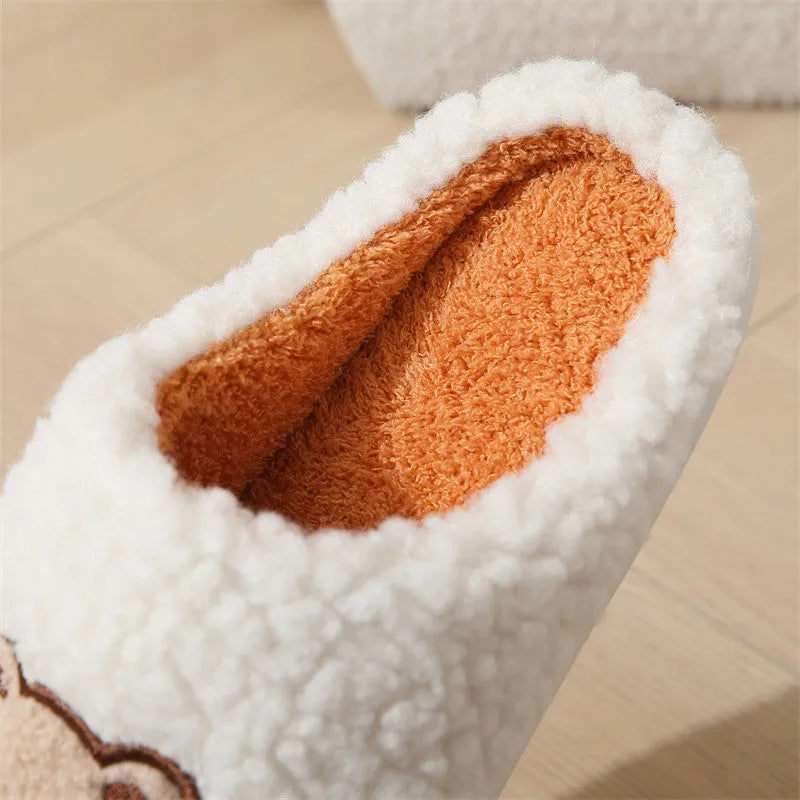 Pair of cute cartoon bear winter slippers with plush upper and non-slip TPR sole on a bedroom floor