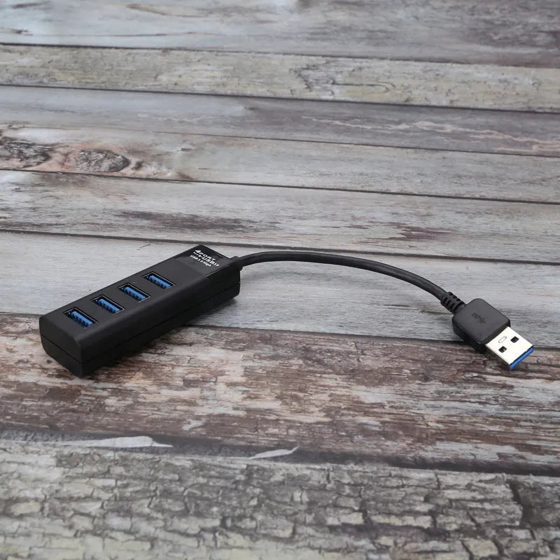 Black USB 3.0 hub with four ports, indicator lights, and a 30cm connecting cable on a desk.