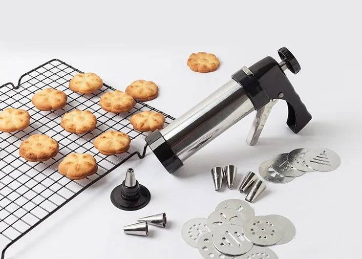 Stainless steel biscuit press gun with assorted cookie moulds and piping nozzles for baking.