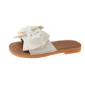 Women's beige suede slip-on sandals with a bow detail and a flat rubber sole.