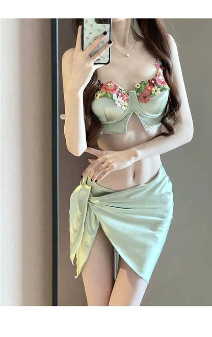Green three-piece women's bikini set with triangle top, briefs, and coordinating skirt on mannequin