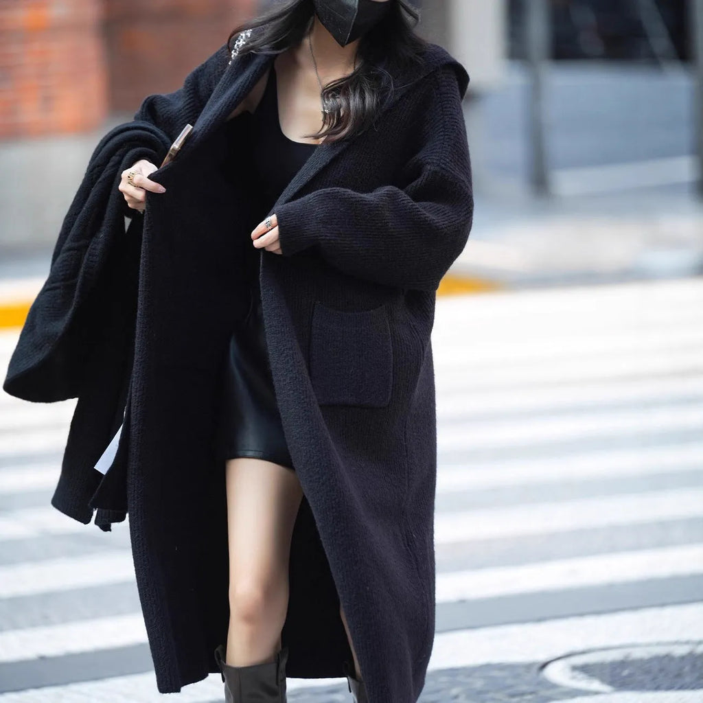 Long grey knitted hooded trench coat on a hanger, showing cardigan front and loose fit.