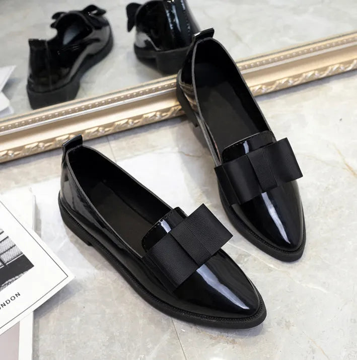 Women's patent leather pointed toe bowtie flats in black on a white background