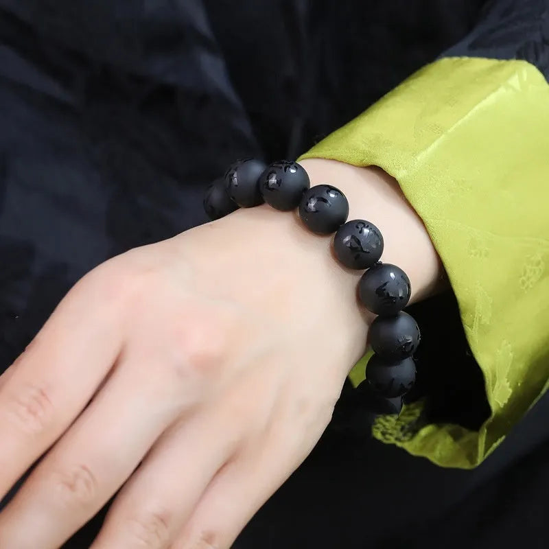 Natural frosted black agate Sanskrit mantra bracelet with Chinese style auspicious patterns on a wrist.