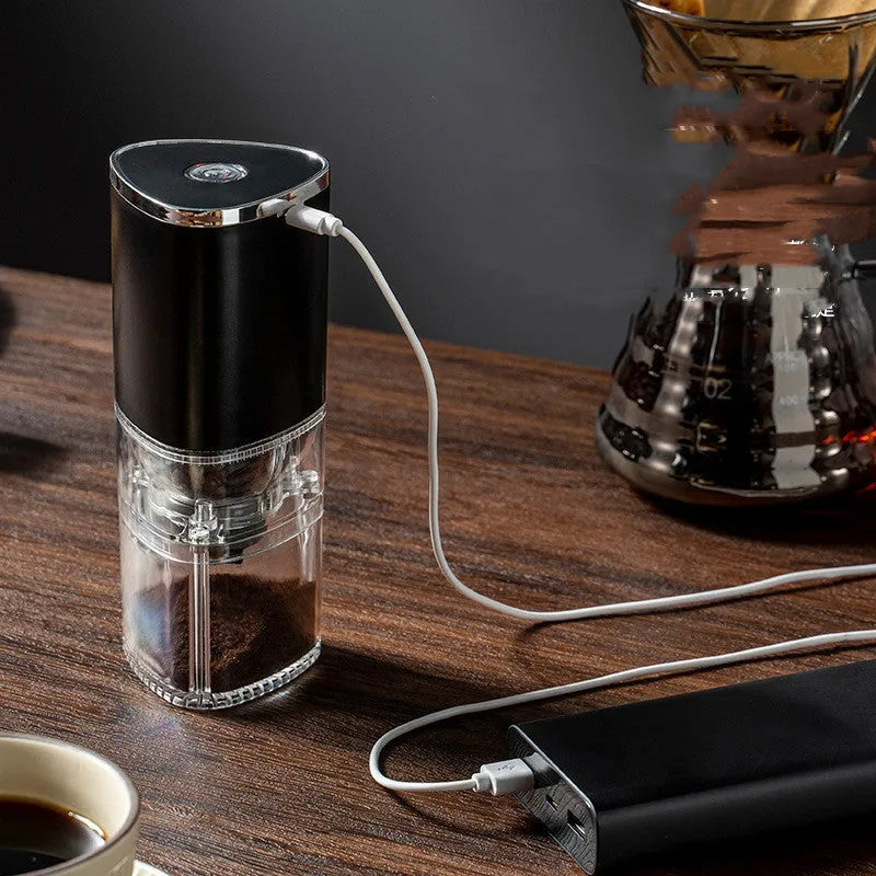 Black and white portable electric coffee grinder with USB charging cable on a kitchen counter.