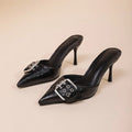 Black women's high heels with pointed toe and ankle strap featuring a decorative buckle.