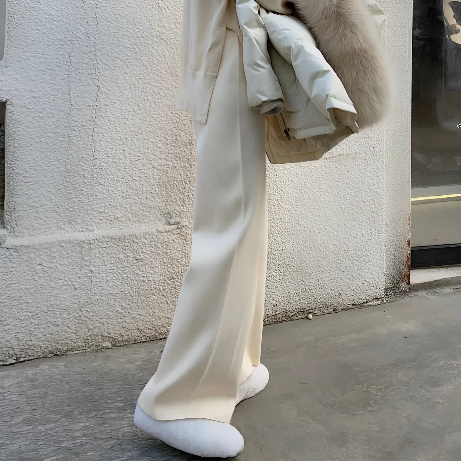 Woman wearing high-waist cream knitted wide-leg trousers with a floor-length, straight-leg silhouette.