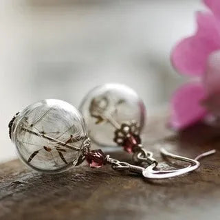 Close-up of transparent glass ball earring with dandelion seed design on a silver French hook.
