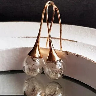 Close-up of transparent glass ball earring with dandelion seed design on a silver French hook.