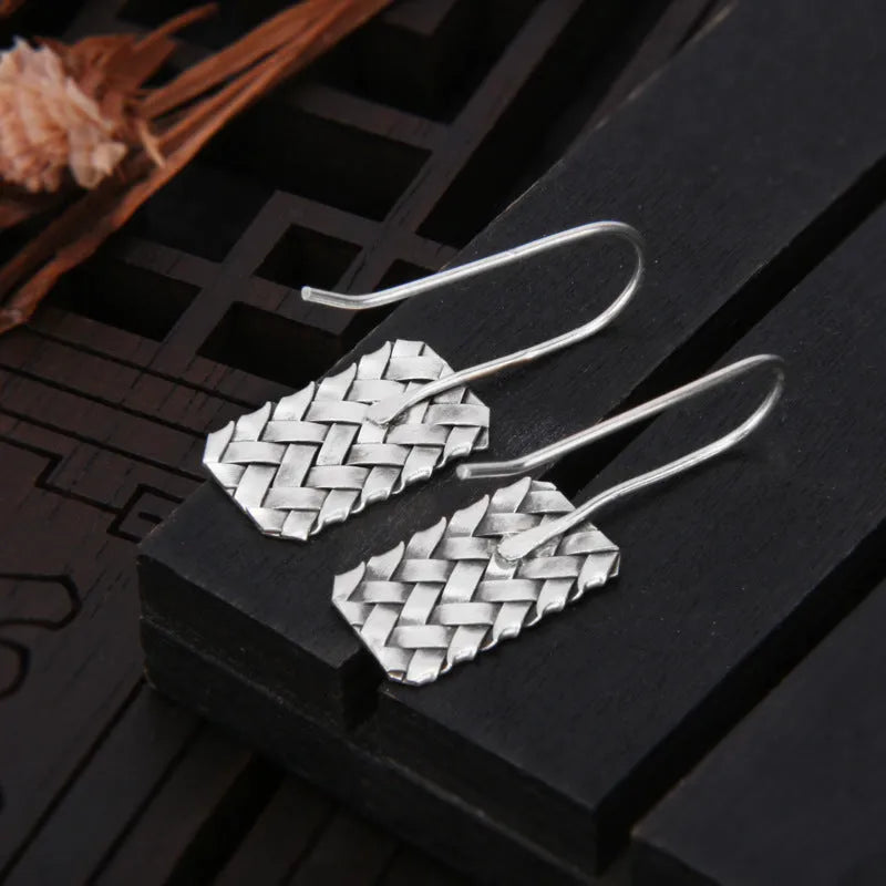 Silver geometric earrings with a woven diamond plaid pattern on a white background.