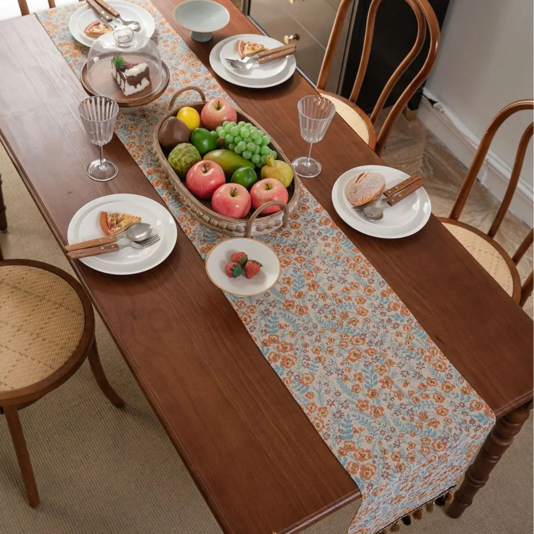 Beige polyester jacquard table runner with long tassels and a floral leaf pattern laid on a table.