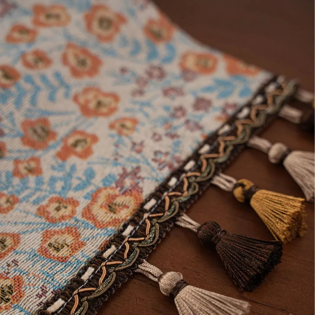 Beige polyester jacquard table runner with long tassels and a floral leaf pattern laid on a table.