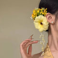 Women's floral tassel side clip hair accessory in purple or yellow on white background.